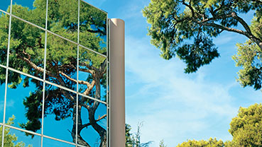 Glass building facade reflecting nearby trees and blue sky.