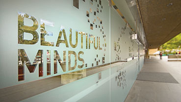 Glass wall with decorative frosted film cutouts displaying the words “BEAUTIFUL MINDS.”